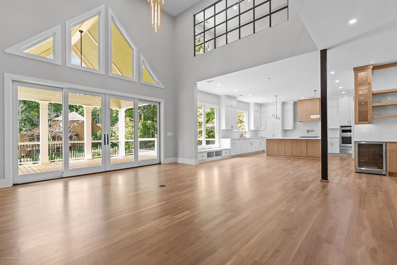 Two-story great room with triangular clerestory windows and glass doors to the covered porch, open to a white kitchen with a natural wood island, Brookcliff new custom home, Marietta, GA