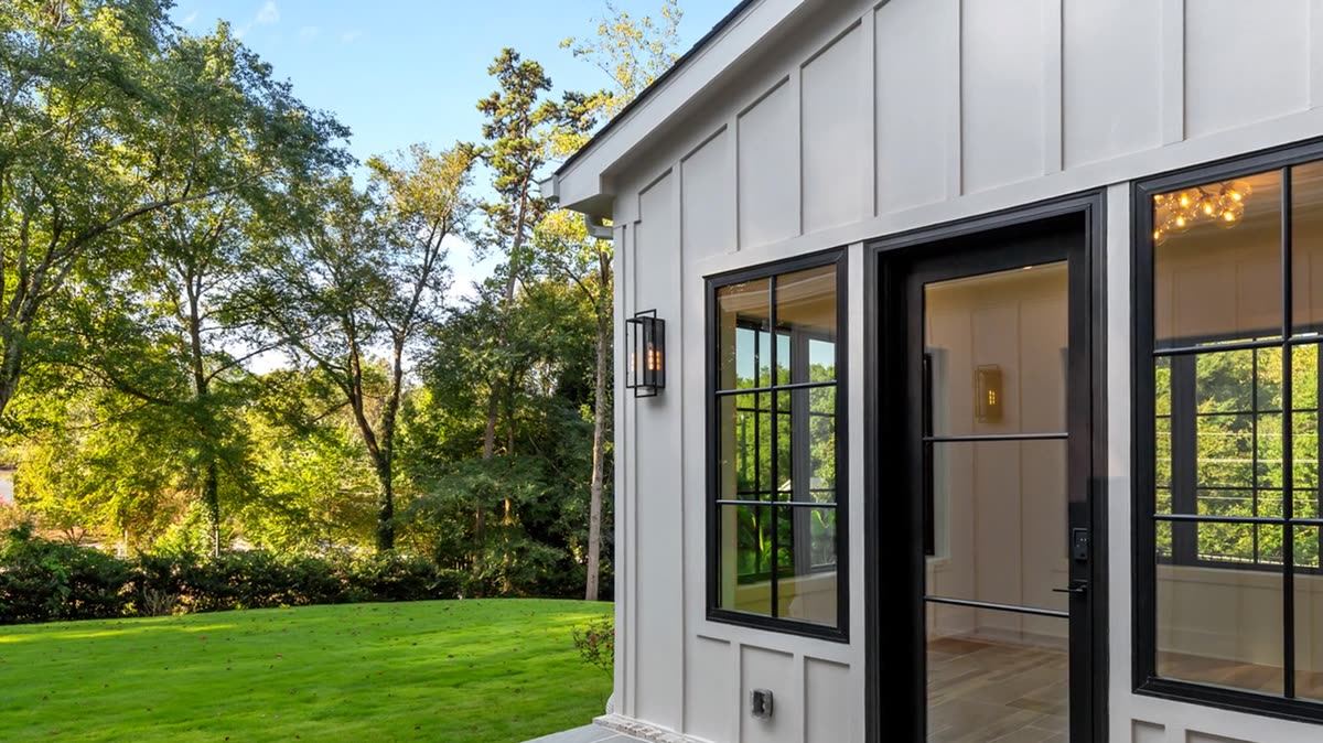 Covered stone patio with board-and-batten siding and black-framed doors facing a wooded lawn, Skylane new custom home, Marietta, GA