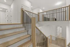 A modern, multi-level stairway with wooden steps and black metal railings graces this luxury home construction, set within a white, well-lit interior space.
