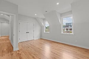 A spacious, empty room with hardwood flooring, white walls, two windows, and a double-door closet.