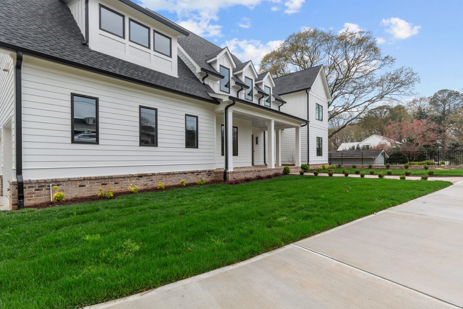 A modern, two-story white house with black-trimmed windows, a neatly manicured lawn, and a concrete driveway. There are shrubs planted along the front of the house.