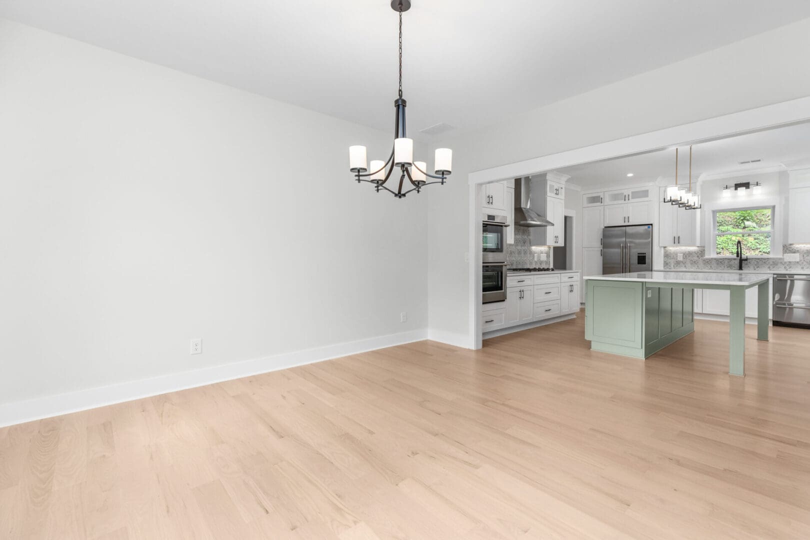 Empty dining room with chandelier and kitchen in background.
