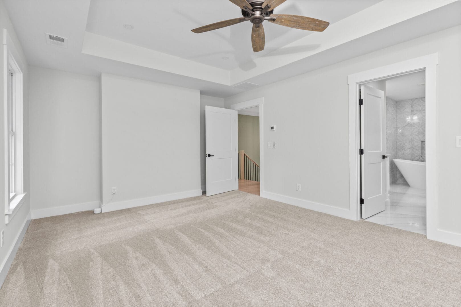 Empty bedroom with ceiling fan and bathroom door.