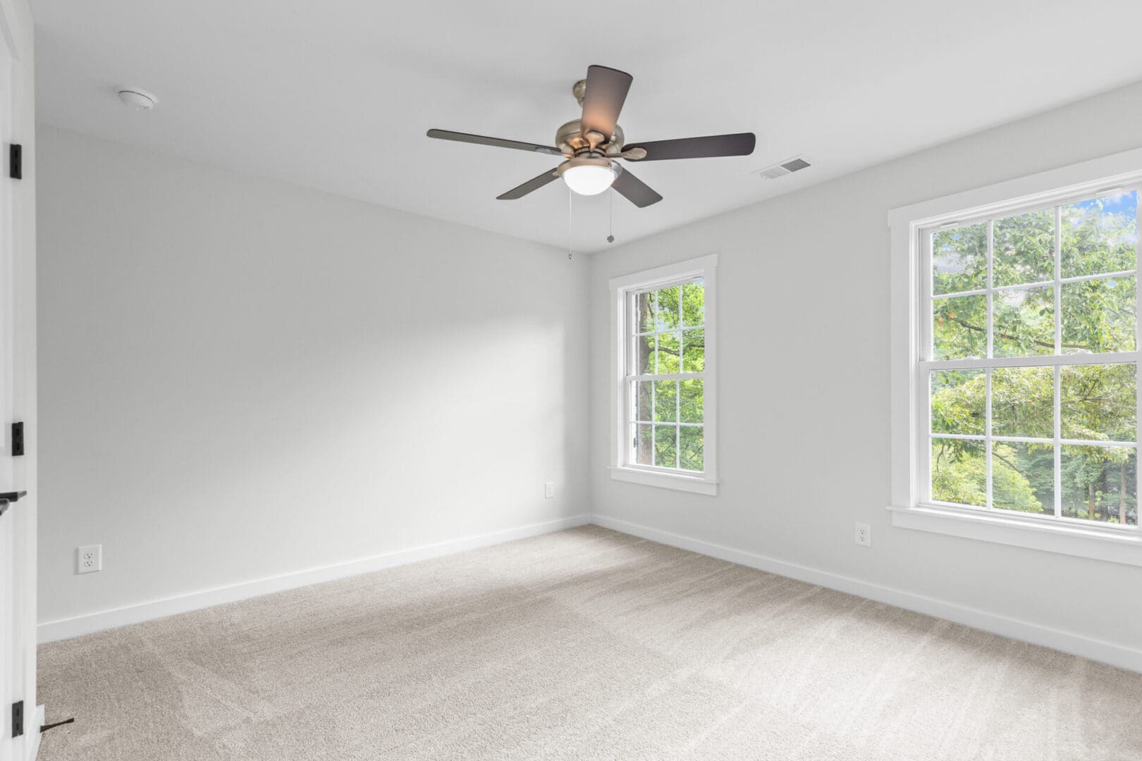 Empty bedroom with ceiling fan and two windows.
