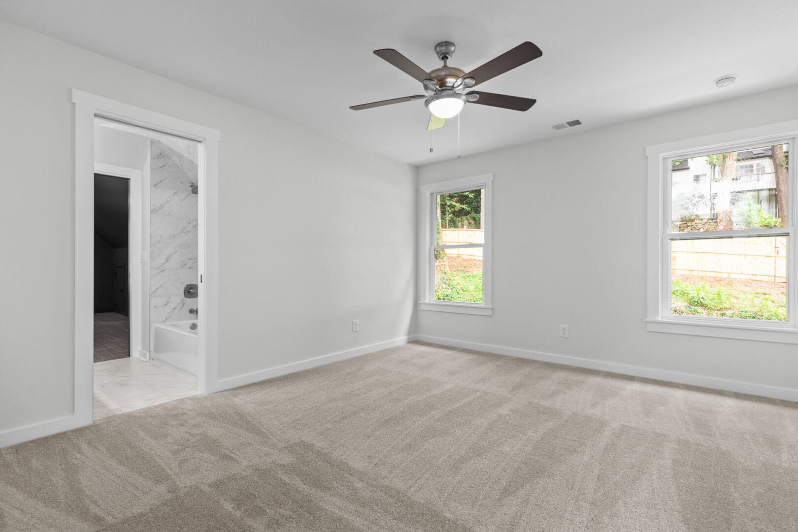Empty bedroom with carpet, windows, and a fan.