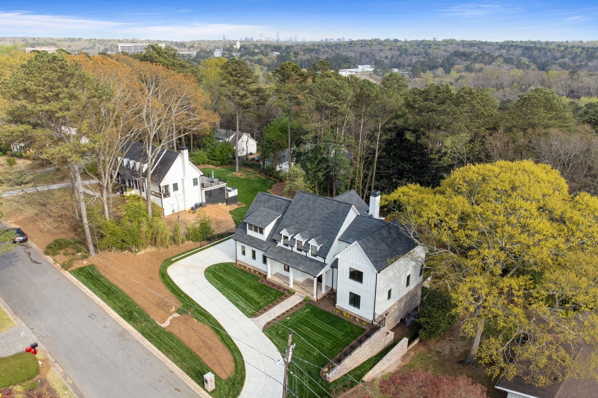 Aerial view of a suburban neighborhood showcasing two large houses with manicured lawns and surrounding trees. A curved driveway leads to one of the houses, and a street runs along the left side.