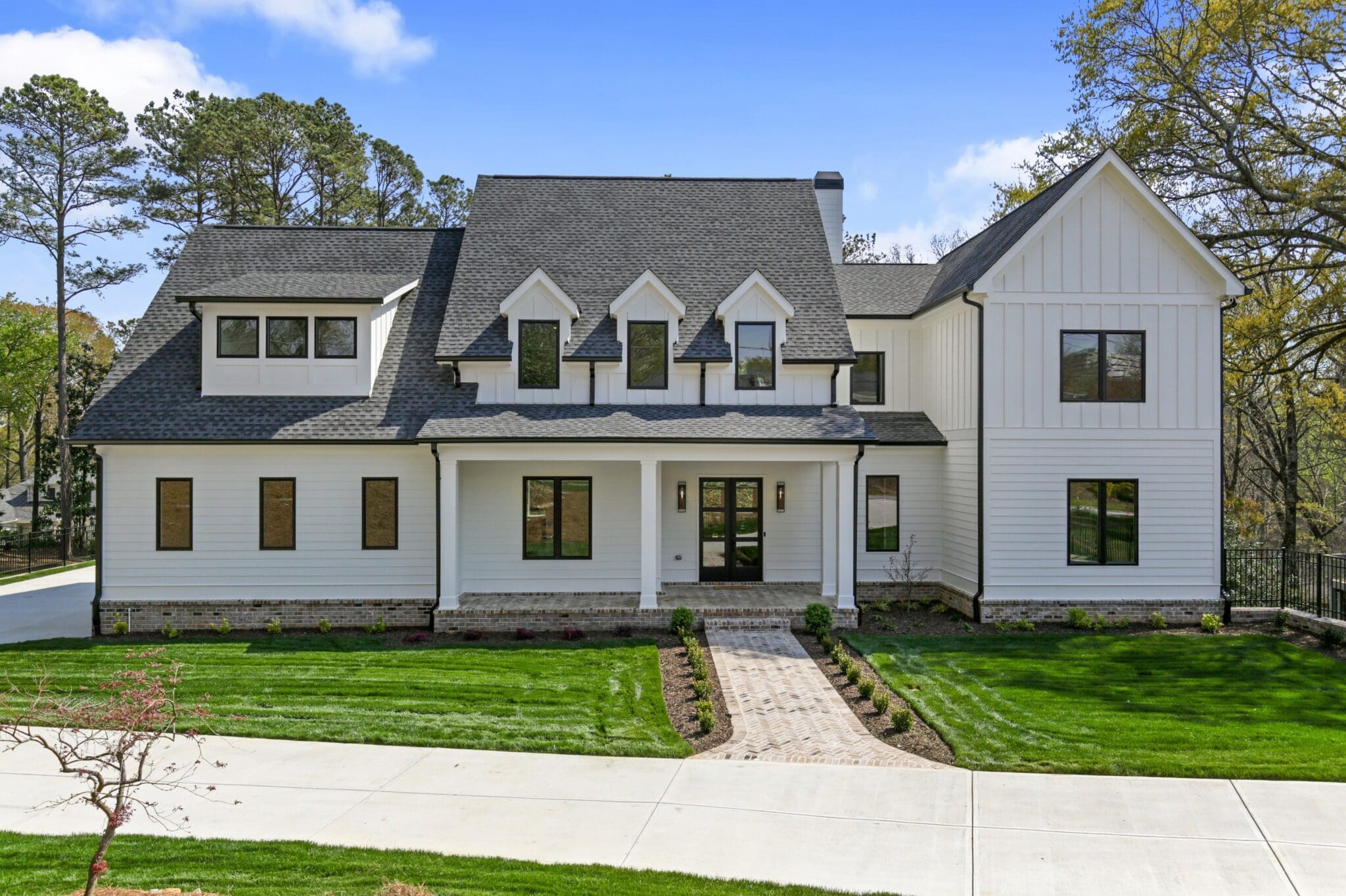 A two-story white house with a dark roof, numerous windows, and well-maintained landscaping, including a stone pathway leading to the front door. Trees are present in the background.