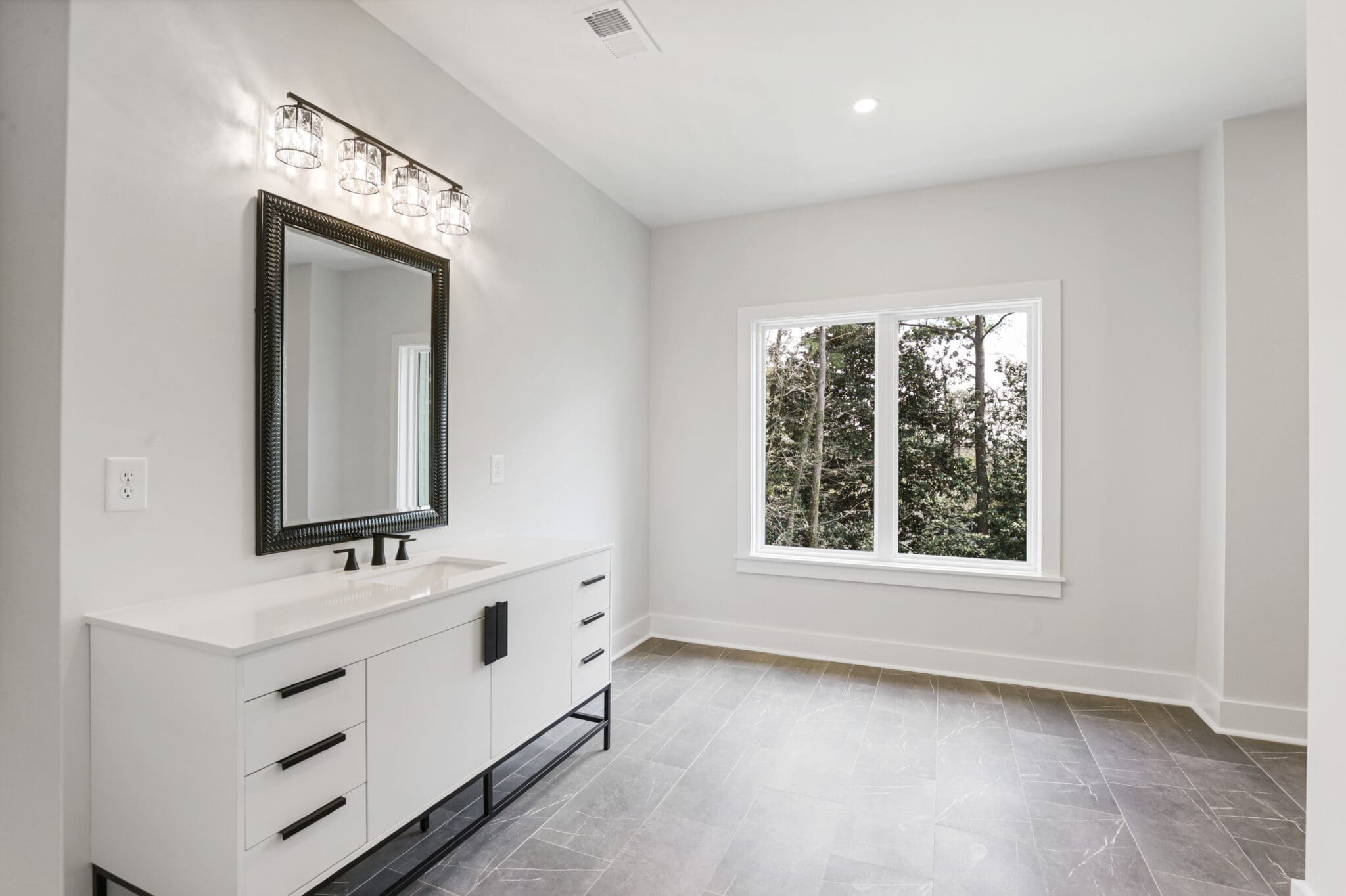 A modern bathroom with a double-sink vanity, rectangular mirror, ceiling light fixture, large window, and gray tile flooring.