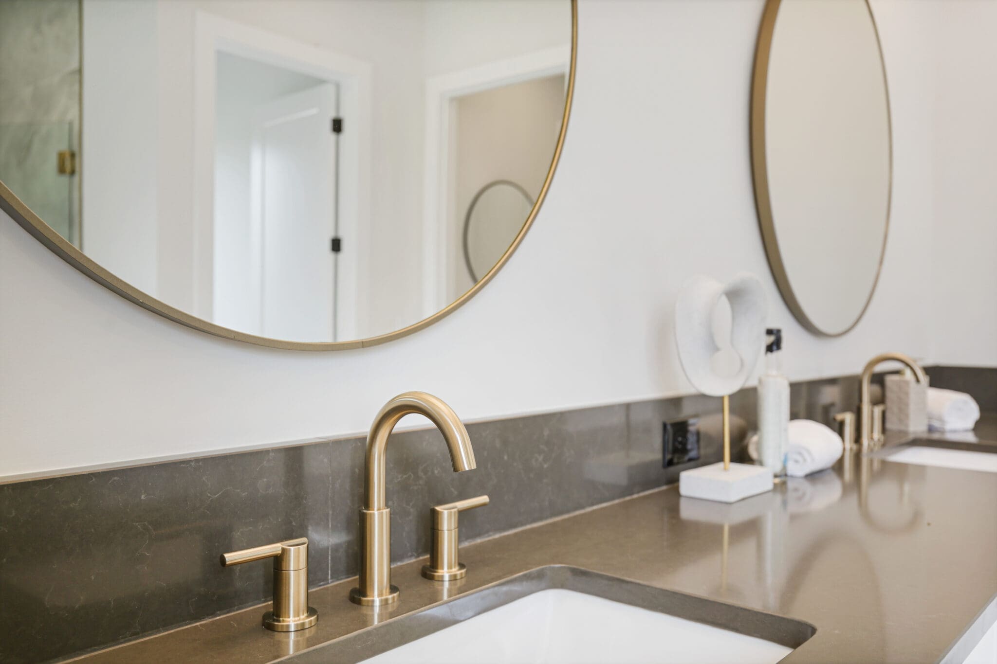 Modern bathroom vanity with dual sinks, gold faucets, large round mirrors, and minimalistic decor.