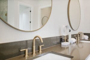 Modern bathroom vanity with dual sinks, gold faucets, large round mirrors, and minimalistic decor.