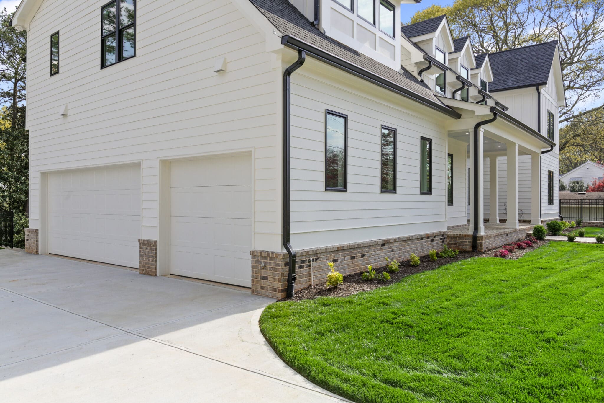 A white, two-story house with black trim features a three-car garage, a covered porch, and a well-maintained lawn and driveway.
