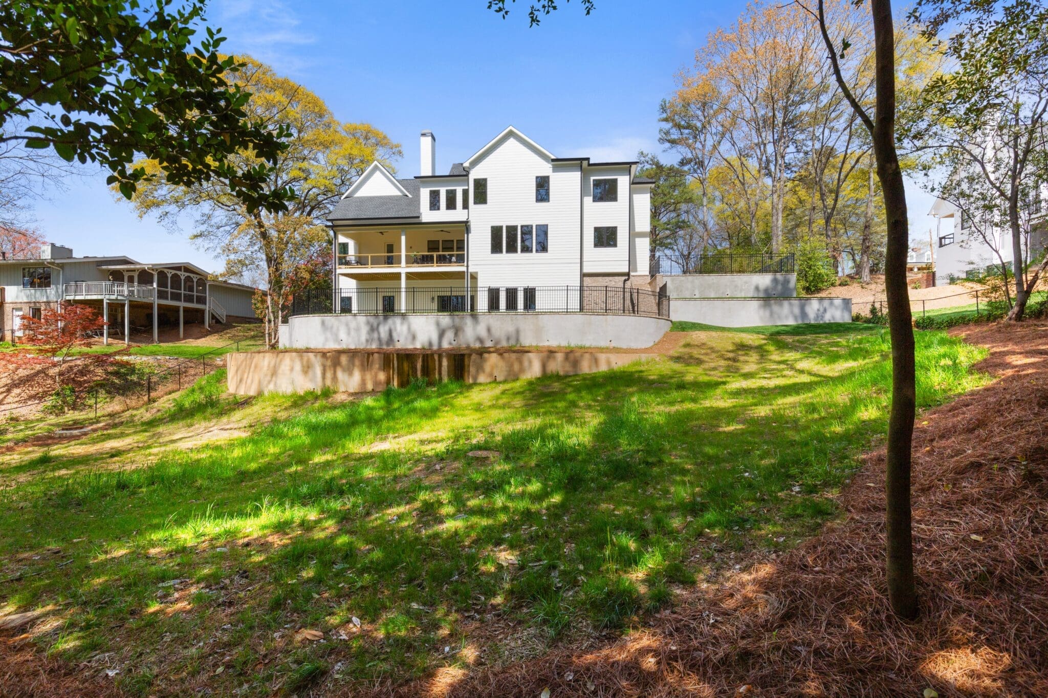 A large white house with multiple stories and a spacious backyard bordered by trees on a sunny day.