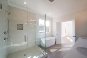 A modern bathroom features a glass-enclosed shower, a freestanding bathtub, dual sinks, and large windows letting in natural light.