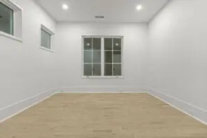 A minimalist empty room with white walls, light wood flooring, and two windows.