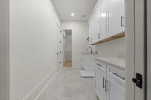 A utility room with white cabinets, a sink, and a washer and dryer. The floor is tiled, and there's a door leading to another room.