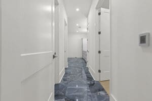 A hallway with white walls and doors, featuring a glossy blue and gray marble-patterned floor, leading to another room visible at the end.