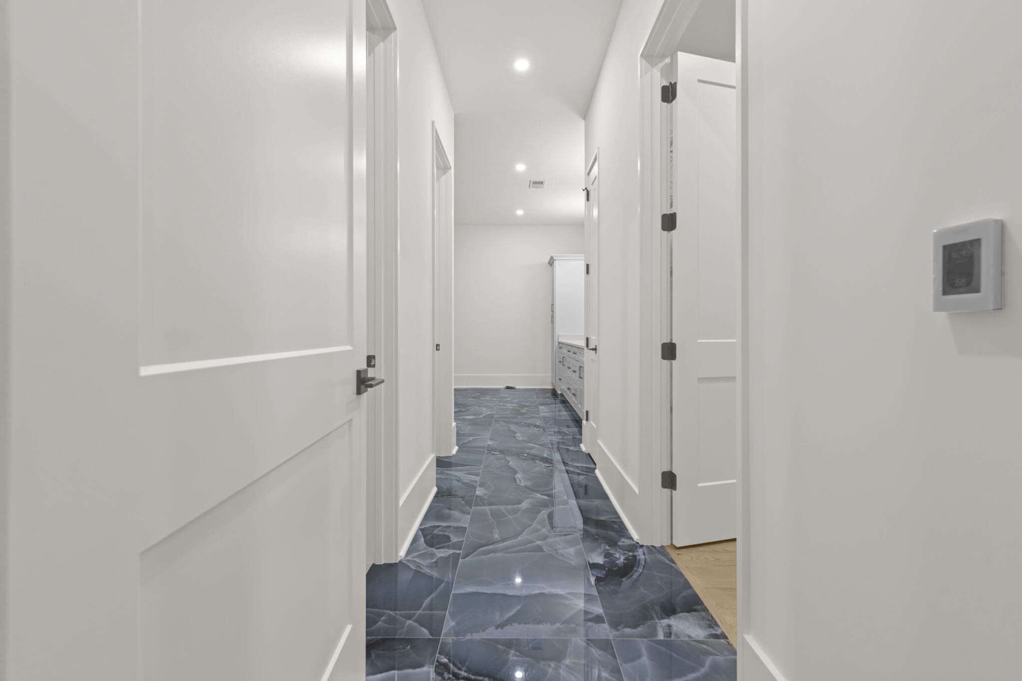 A well-lit hallway with white walls and doors, featuring a polished dark blue marble floor.