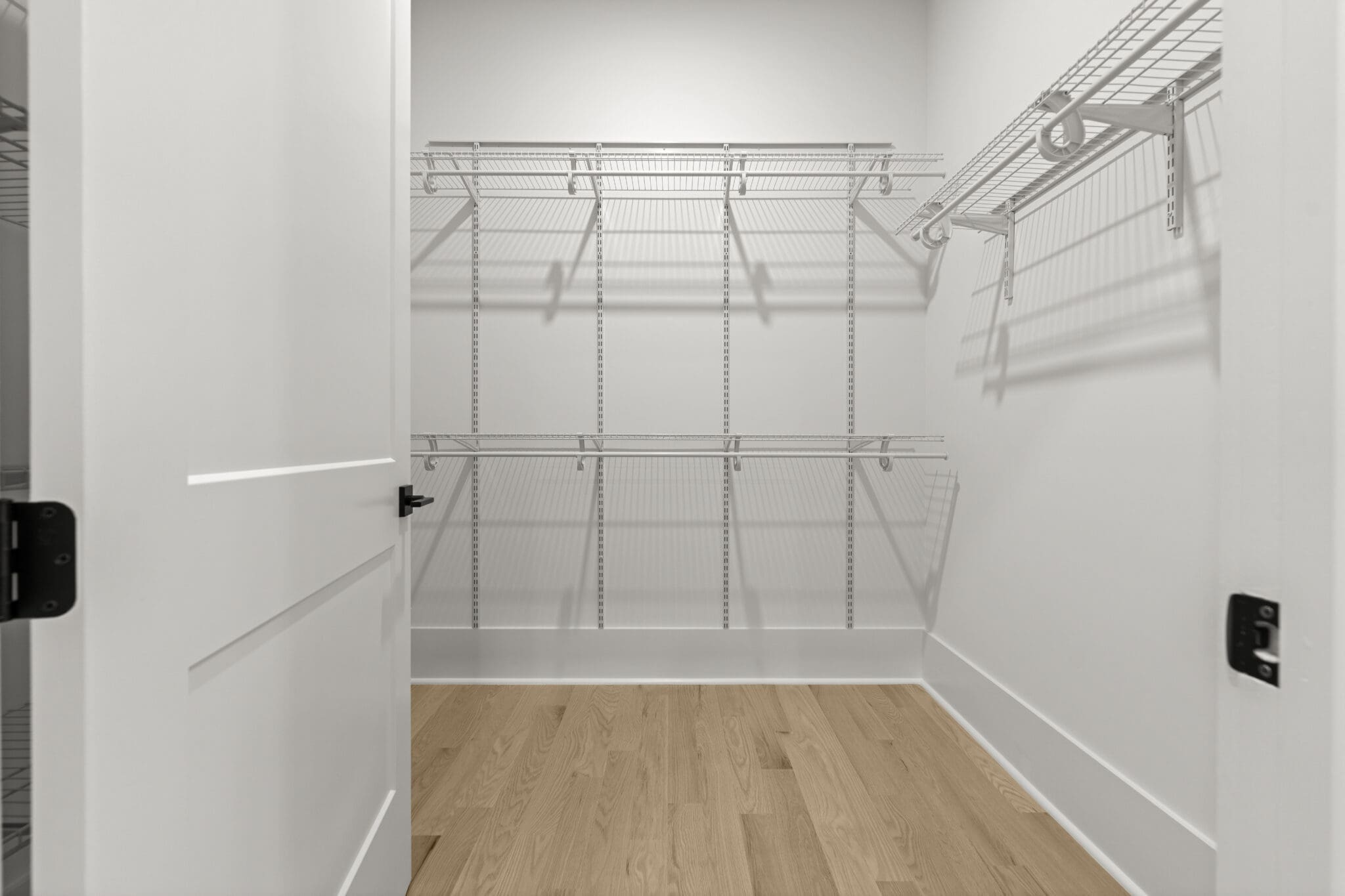 A walk-in closet with empty wire shelving on the walls and a hardwood floor. The door is partially open.