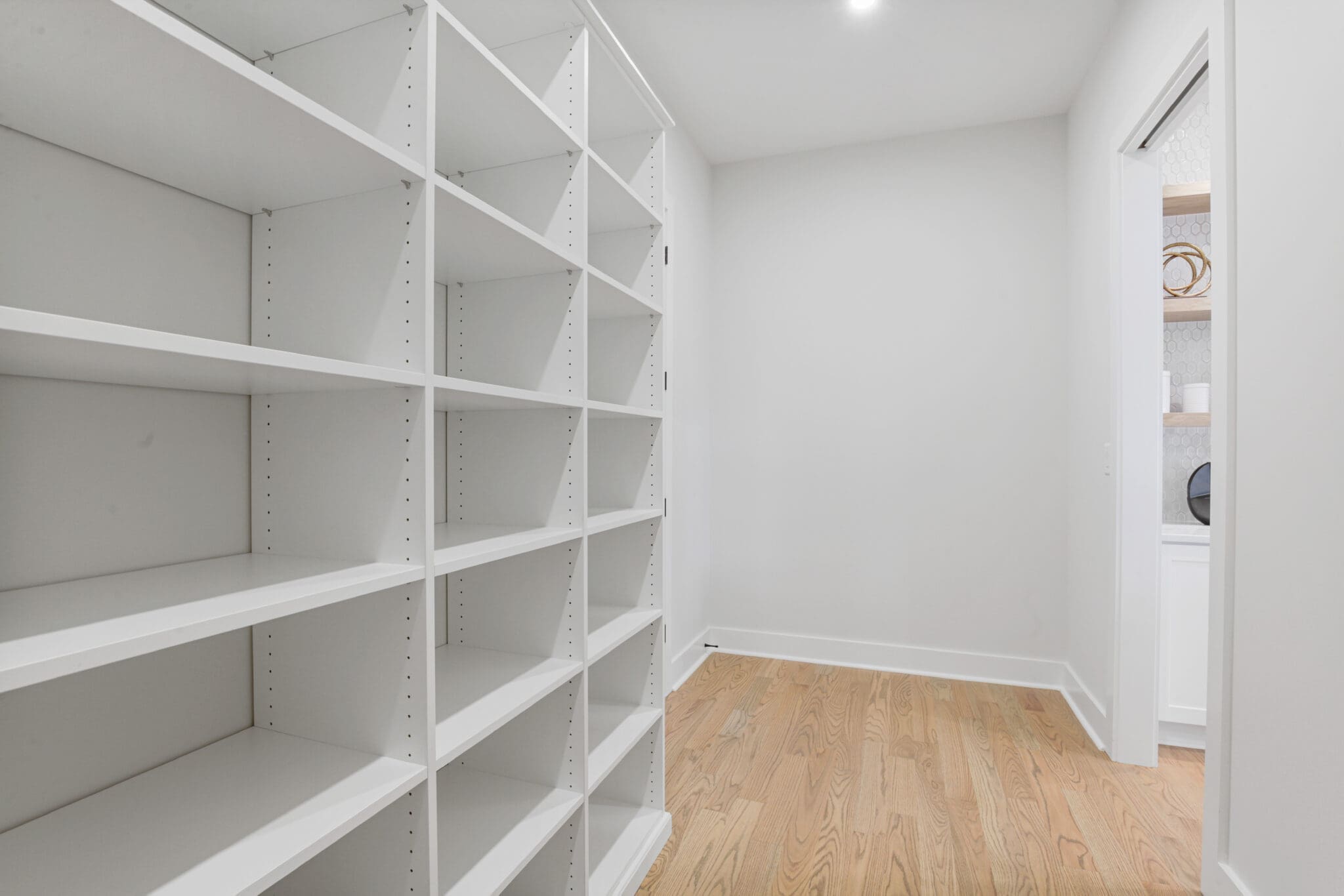 A narrow, empty walk-in closet with white shelving units on the left and a wooden floor.