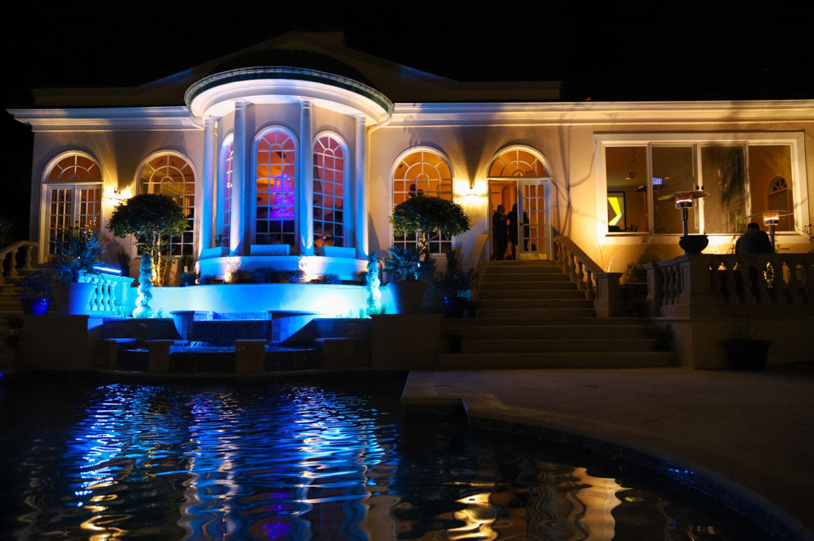 Nighttime view of a mansion with a pool.
